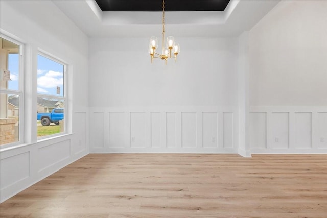 unfurnished dining area with a chandelier, a decorative wall, a raised ceiling, and light wood-style floors