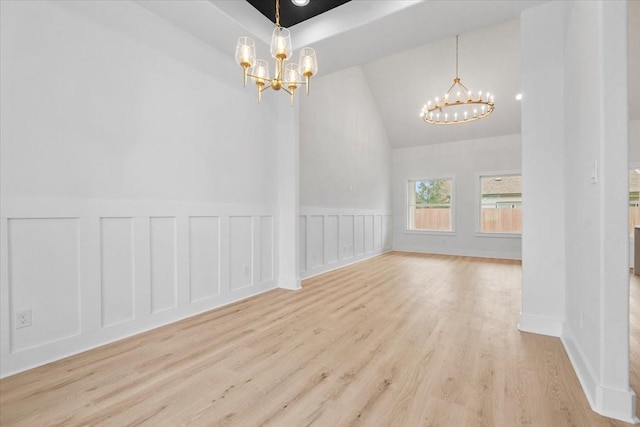 spare room with vaulted ceiling, a decorative wall, a notable chandelier, and wood finished floors