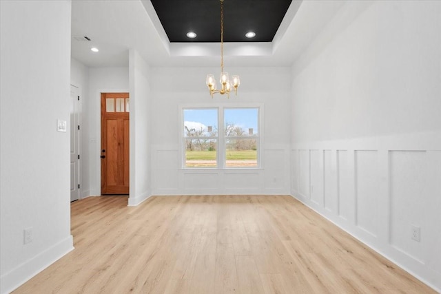 spare room with wood finished floors, recessed lighting, a decorative wall, a raised ceiling, and a chandelier