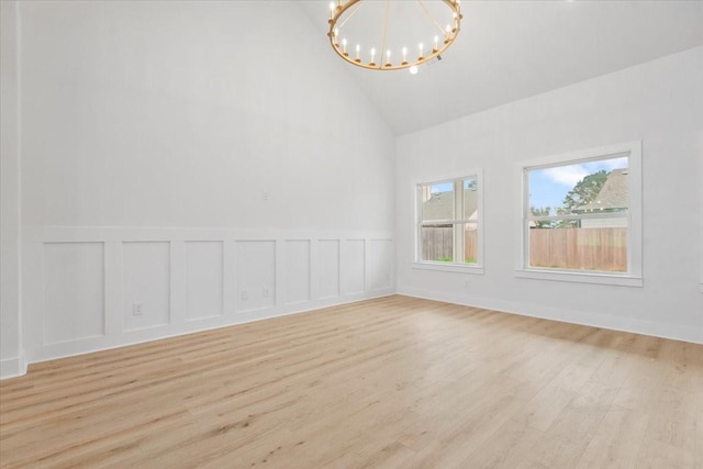 unfurnished room with an inviting chandelier, light wood-style flooring, a wainscoted wall, and high vaulted ceiling