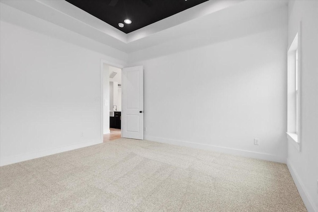 spare room featuring a tray ceiling, recessed lighting, light colored carpet, and baseboards