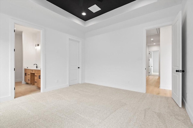 unfurnished bedroom with ensuite bath, recessed lighting, a raised ceiling, light colored carpet, and attic access