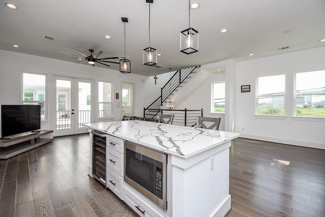 kitchen featuring built in microwave, white cabinetry, a center island, hanging light fixtures, and beverage cooler