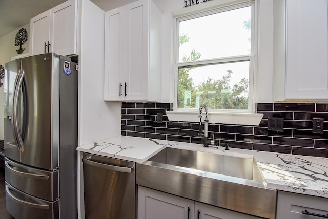 kitchen with sink, appliances with stainless steel finishes, white cabinetry, tasteful backsplash, and light stone countertops