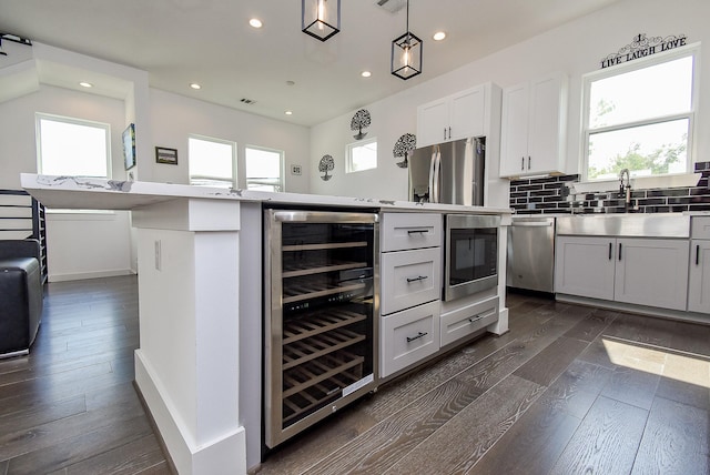 kitchen with a healthy amount of sunlight, stainless steel appliances, beverage cooler, and white cabinets