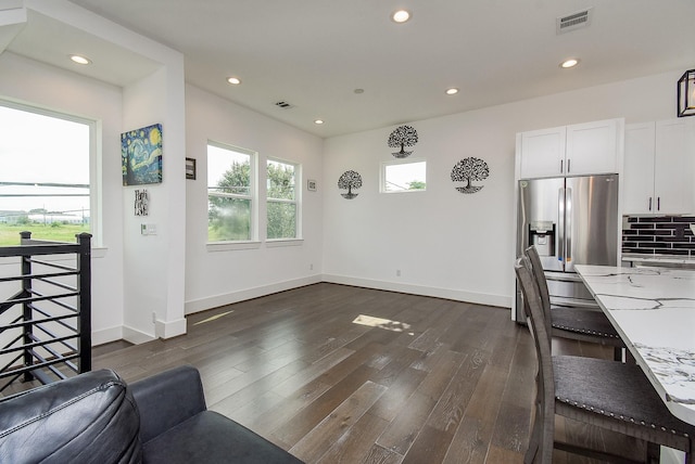 interior space featuring stainless steel refrigerator with ice dispenser, light stone counters, tasteful backsplash, white cabinets, and dark hardwood / wood-style flooring