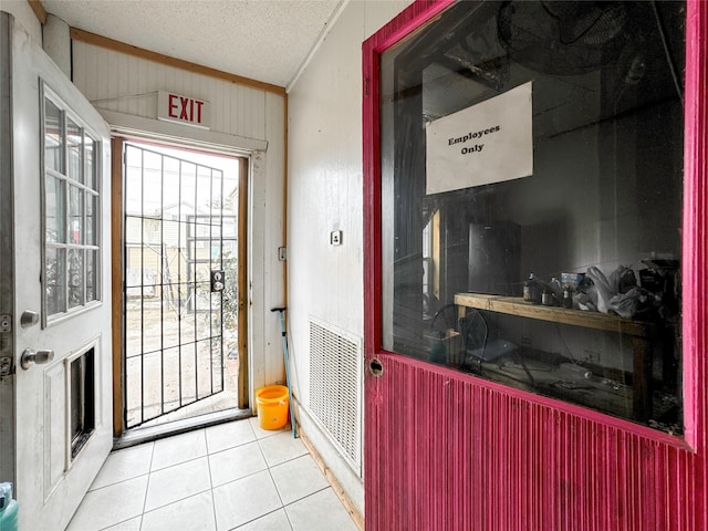 doorway to outside featuring a textured ceiling, light tile patterned flooring, and crown molding