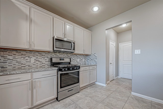 kitchen featuring stainless steel appliances, light tile patterned floors, tasteful backsplash, light stone counters, and white cabinets