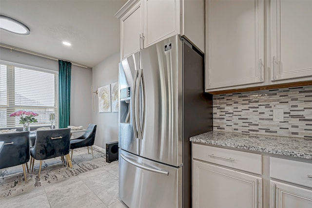 kitchen featuring decorative backsplash, light stone countertops, white cabinets, stainless steel fridge with ice dispenser, and light tile patterned flooring