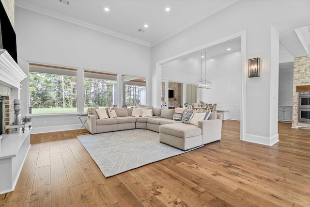 living room with a high ceiling, a notable chandelier, wood-type flooring, a fireplace, and ornamental molding