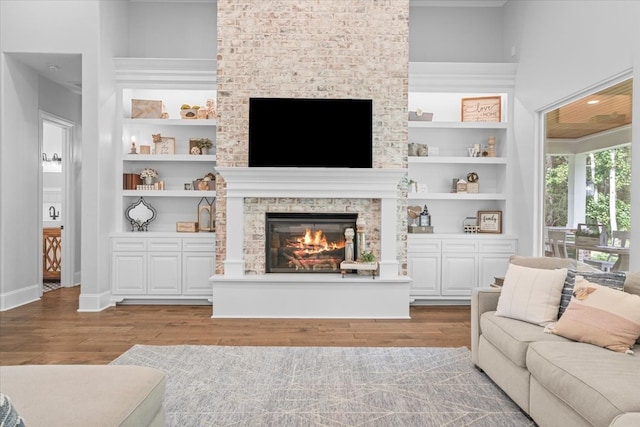 living room with hardwood / wood-style flooring, a stone fireplace, built in features, and a towering ceiling