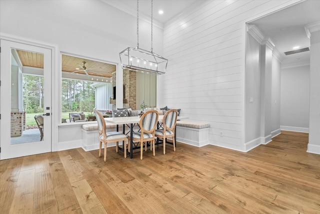 dining room with light hardwood / wood-style flooring, ceiling fan, ornamental molding, and wood walls