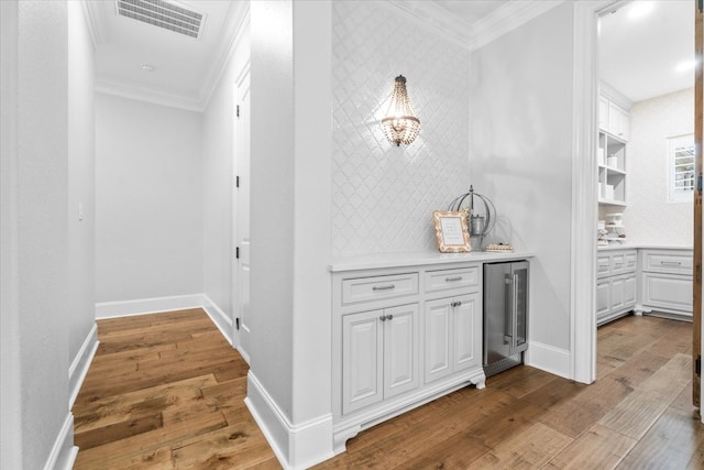 corridor with hardwood / wood-style floors, crown molding, and beverage cooler