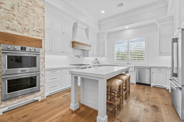 kitchen with a kitchen breakfast bar, white cabinets, custom range hood, and appliances with stainless steel finishes