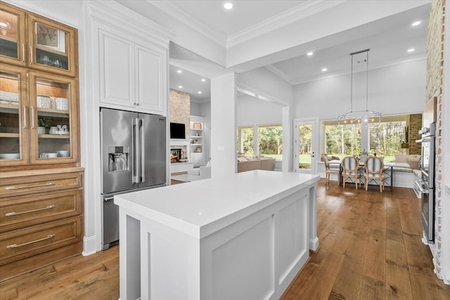 kitchen featuring hardwood / wood-style floors, a center island, white cabinets, a large fireplace, and stainless steel appliances