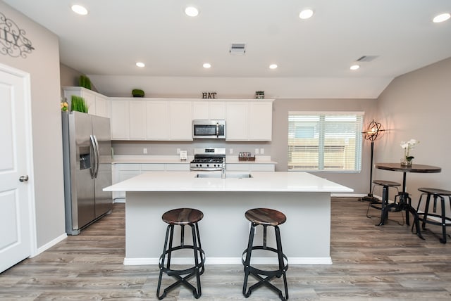 kitchen with a center island with sink, white cabinets, light hardwood / wood-style flooring, and appliances with stainless steel finishes