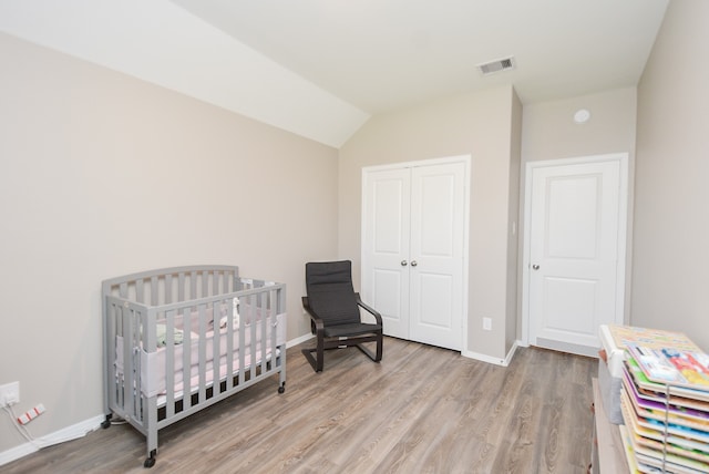 bedroom featuring a closet, lofted ceiling, light hardwood / wood-style flooring, and a nursery area