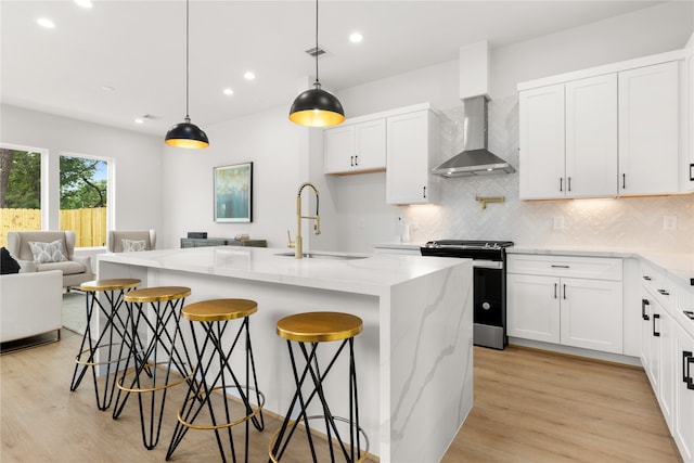 kitchen with light stone countertops, stainless steel range, sink, wall chimney range hood, and a center island with sink