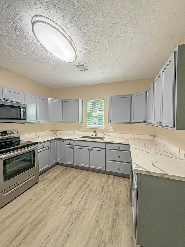 304 E Caroline St, Trinity, TX 75862 - kitchen featuring a textured ceiling, stainless steel appliances, gray cabinets, and light hardwood / wood-style floors