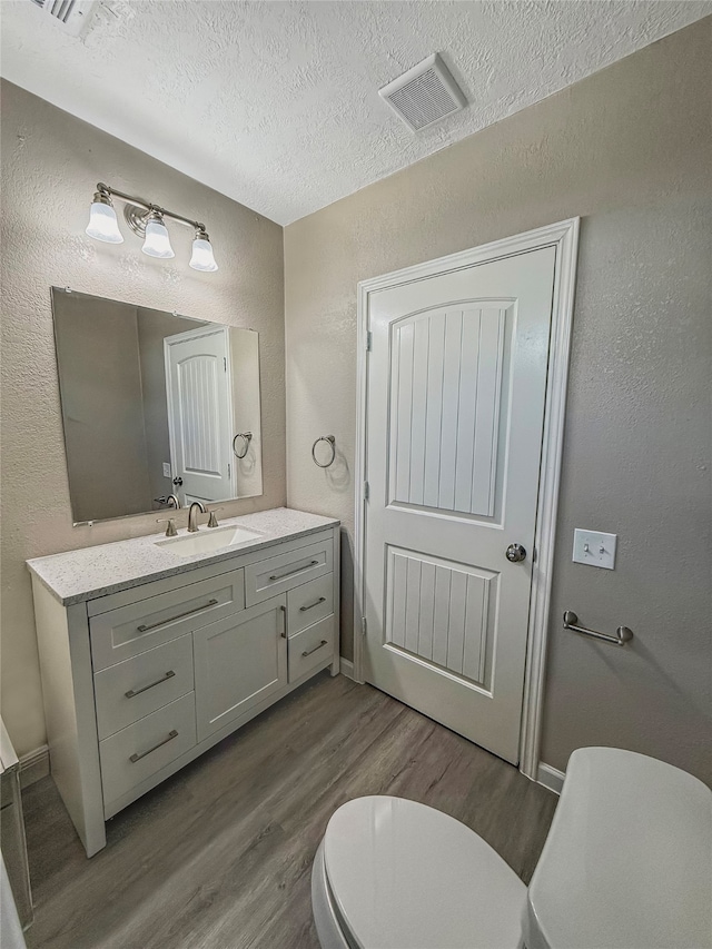 bathroom featuring vanity, wood-type flooring, a textured ceiling, and toilet