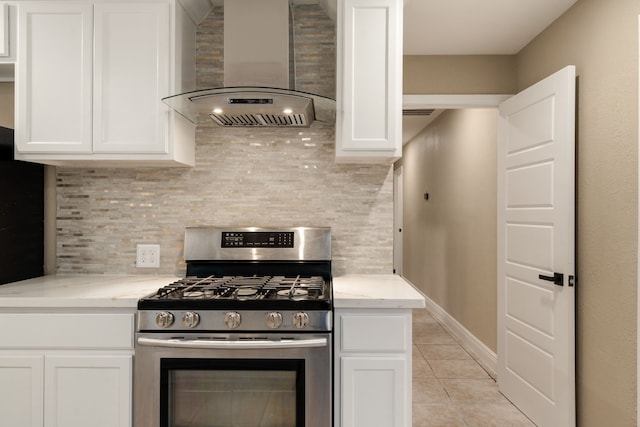 kitchen with stainless steel gas range, white cabinets, light stone countertops, and wall chimney range hood