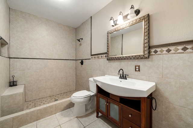 bathroom featuring vanity, tile patterned floors, toilet, tiled shower, and tile walls