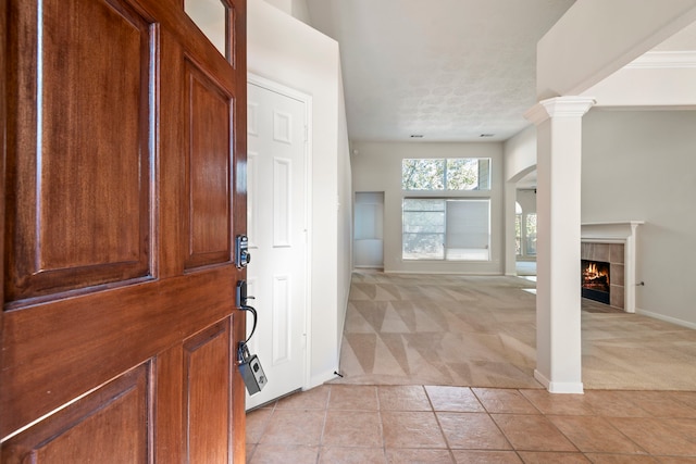 foyer entrance featuring decorative columns, a tile fireplace, light carpet, and a textured ceiling