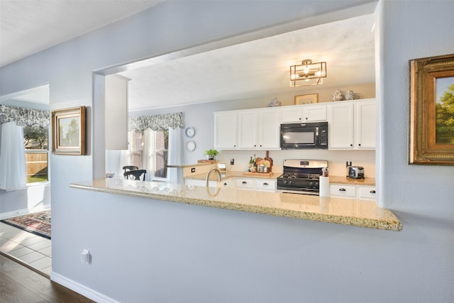 kitchen with light stone countertops, kitchen peninsula, dark hardwood / wood-style flooring, gas range, and white cabinetry