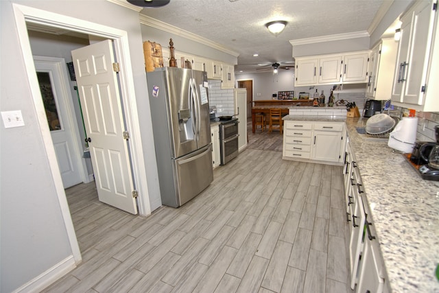 kitchen featuring decorative backsplash, ornamental molding, stainless steel appliances, ceiling fan, and light hardwood / wood-style floors