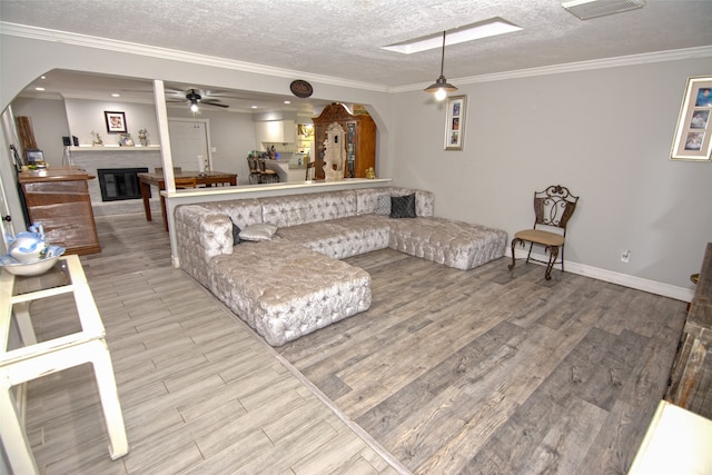 living room with a textured ceiling, light wood-type flooring, ceiling fan, and crown molding