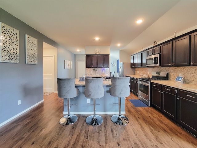 kitchen featuring a center island, light hardwood / wood-style flooring, decorative backsplash, appliances with stainless steel finishes, and a kitchen bar