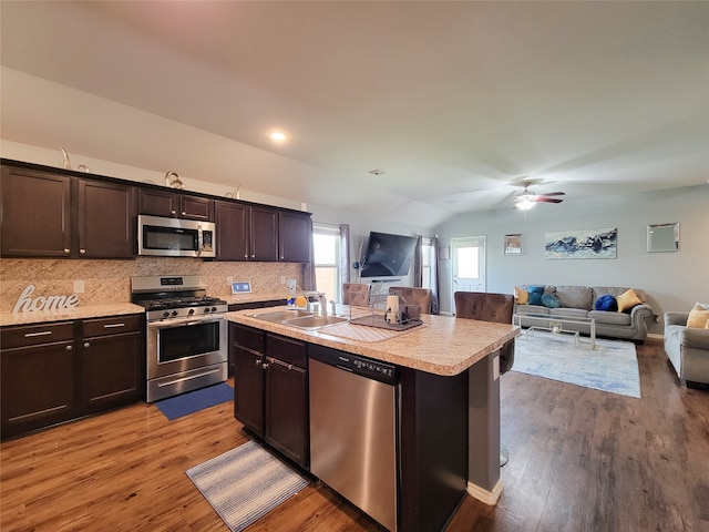 kitchen with lofted ceiling, backsplash, a center island with sink, light hardwood / wood-style flooring, and appliances with stainless steel finishes