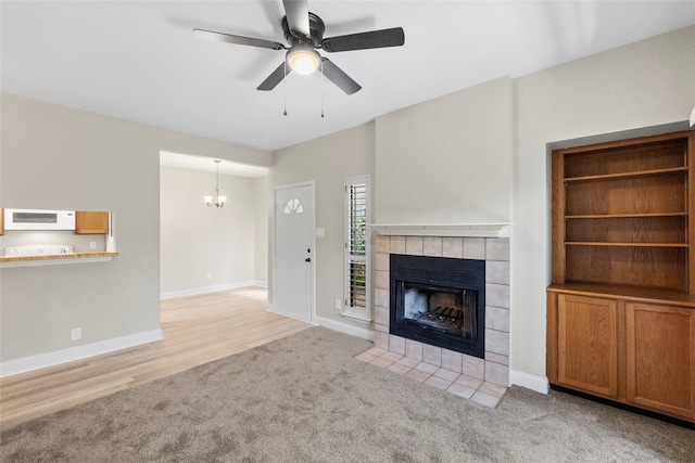 unfurnished living room featuring ceiling fan with notable chandelier, light hardwood / wood-style floors, and a fireplace