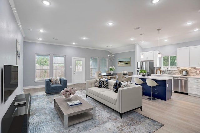 living room featuring a chandelier, sink, light hardwood / wood-style floors, and ornamental molding