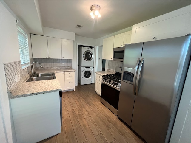 kitchen featuring sink, hardwood / wood-style flooring, stacked washing maching and dryer, appliances with stainless steel finishes, and white cabinetry