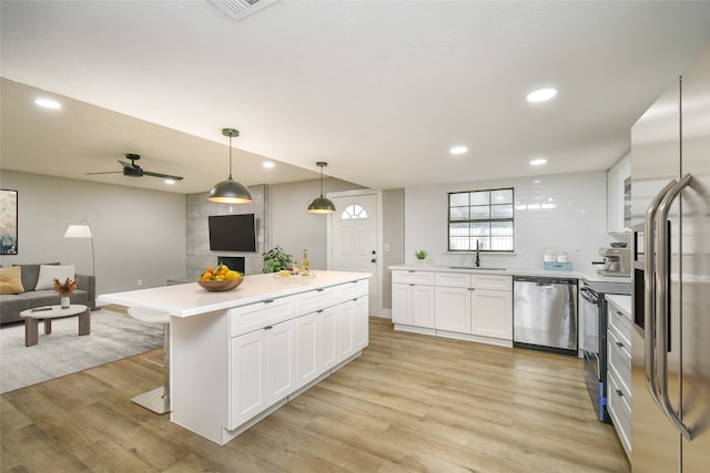 kitchen with pendant lighting, sink, appliances with stainless steel finishes, light hardwood / wood-style floors, and white cabinetry