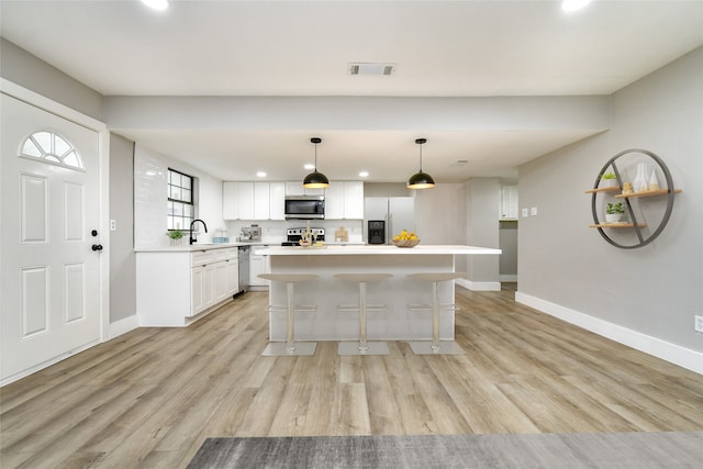 kitchen with pendant lighting, white cabinets, light wood-type flooring, appliances with stainless steel finishes, and a kitchen island