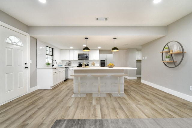 kitchen with pendant lighting, white cabinetry, a kitchen island, light hardwood / wood-style floors, and stainless steel appliances