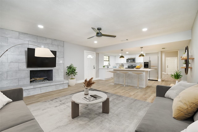 living room featuring a fireplace, ceiling fan, and light hardwood / wood-style flooring