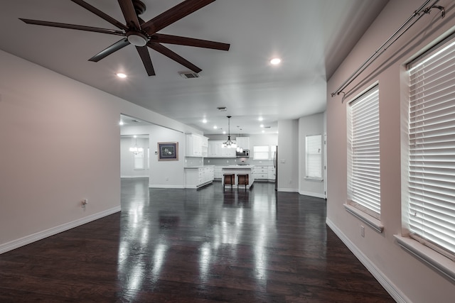 unfurnished living room featuring dark hardwood / wood-style flooring and ceiling fan with notable chandelier