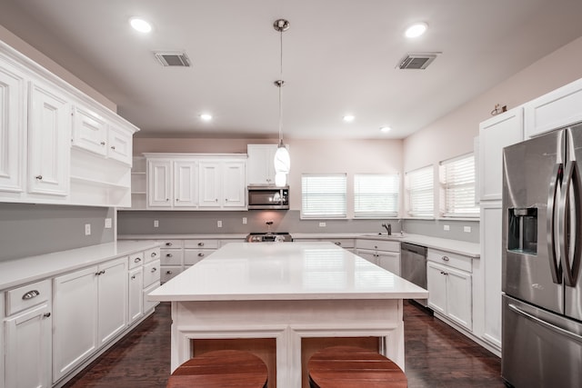 kitchen with hanging light fixtures, stainless steel appliances, white cabinets, and a kitchen island