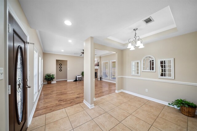 entrance foyer with ceiling fan with notable chandelier, light wood-type flooring, a raised ceiling, and ornamental molding