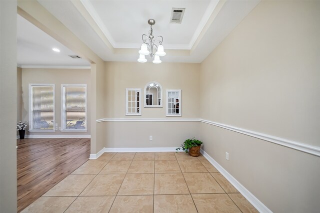 unfurnished dining area featuring a tray ceiling, light hardwood / wood-style flooring, a chandelier, and ornamental molding