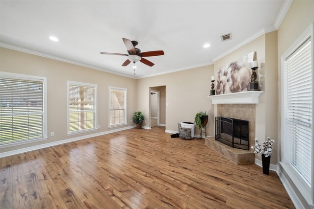 unfurnished living room with a tile fireplace, ceiling fan, wood-type flooring, and ornamental molding