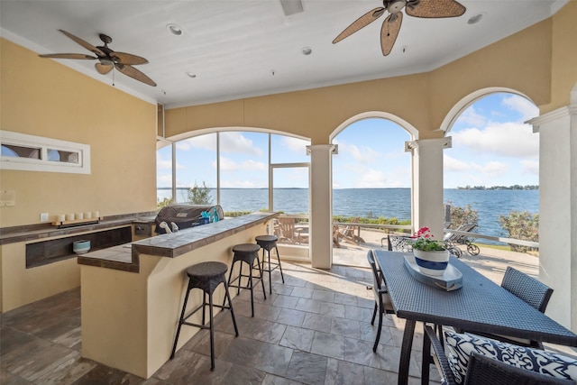 interior space featuring ceiling fan, a water view, exterior bar, and an outdoor kitchen