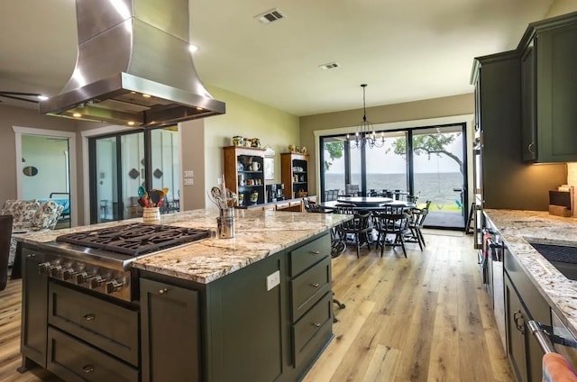 kitchen with island exhaust hood, pendant lighting, a water view, light hardwood / wood-style flooring, and a center island with sink