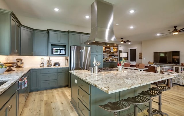 kitchen with light stone counters, stainless steel appliances, island range hood, a center island, and light hardwood / wood-style floors