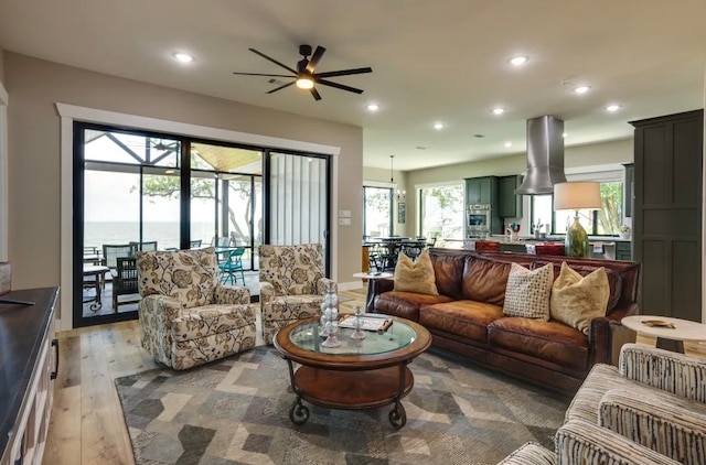 living room featuring light wood-type flooring, a water view, plenty of natural light, and ceiling fan