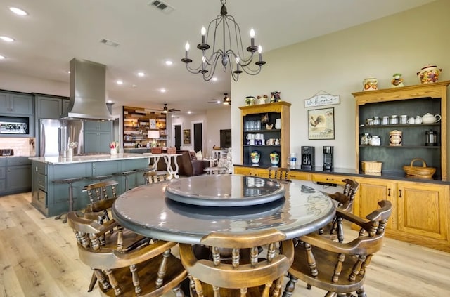 dining area with ceiling fan with notable chandelier and light hardwood / wood-style flooring