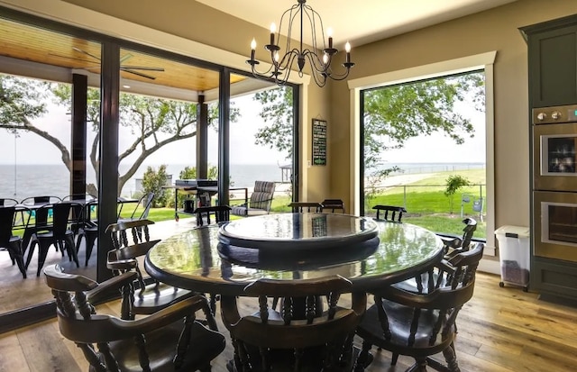 dining space featuring light hardwood / wood-style flooring, a water view, and an inviting chandelier